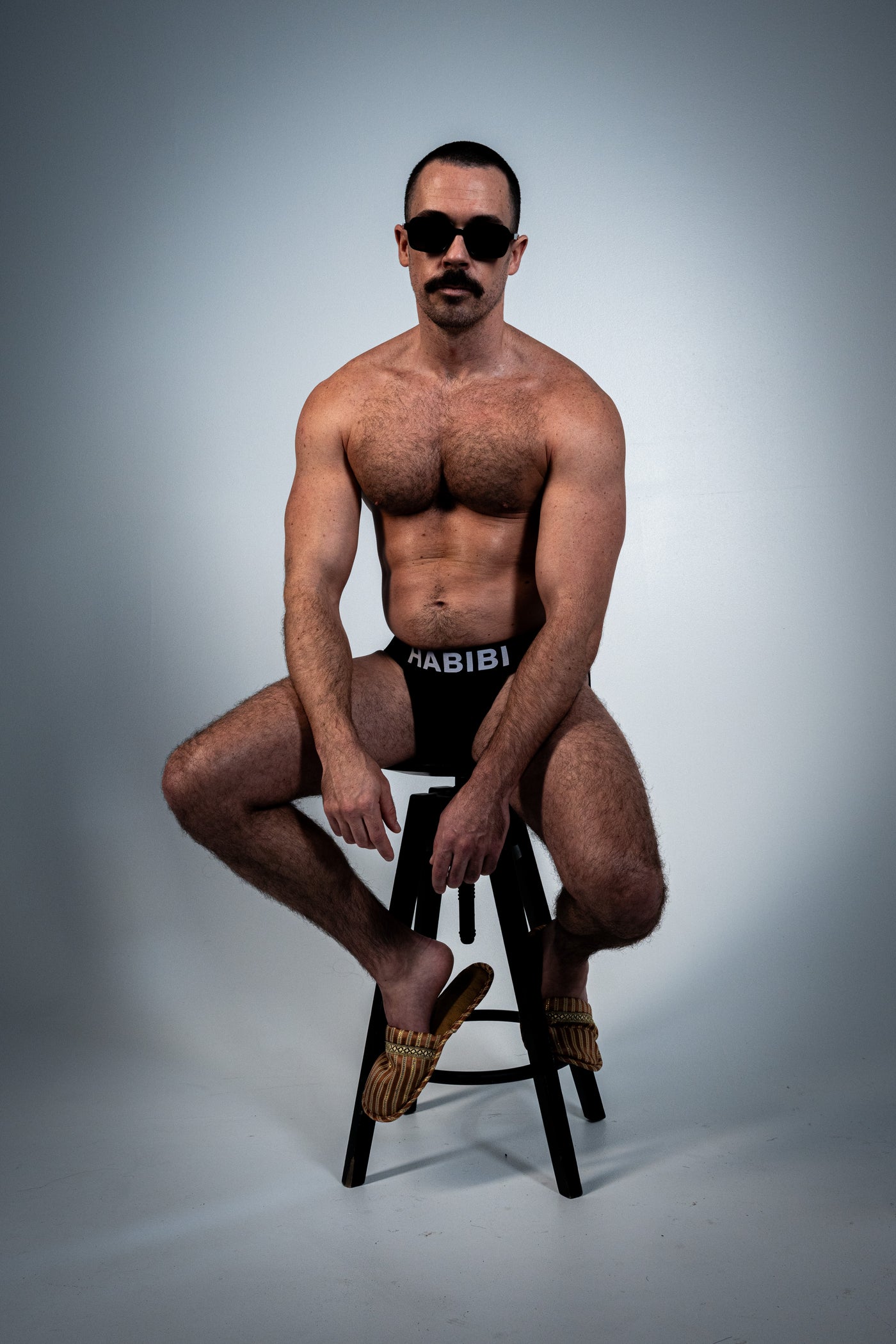 Black 3EIB English jockstrap with white HABIBI lettering, front fit on a seated model