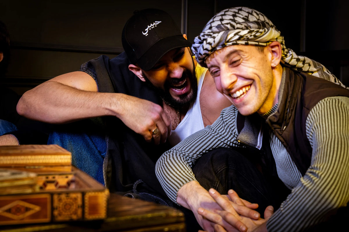 Two people laughing together, with a Habibi cap visible